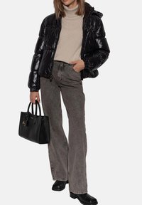 Giacca a vento nera con finitura lucida, dolcevita beige, jeans grigi a gamba svasata, borsa nera e stivali neri con tacco.
