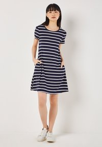 Maritimer gestreifter Kleid aus weichem Jersey-Stoff, mit einem lockeren Schnitt, Rundhalsausschnitt, kurzen Ärmeln und seitlichen Taschen. Kombiniert mit weißen Sneakers.