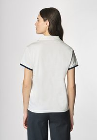 Polo bianco con colletto, dettagli a coste blu navy sulle maniche e aperture laterali, realizzato in un tessuto liscio e leggero.