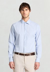 Light blue, long-sleeved dress shirt with fine white stripes, buttoned front, classic collar, paired with beige trousers and a brown belt.