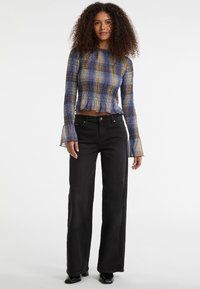 Blauw en geel patroon top met smockstructuur, lange uitlopende mouwen en een gerimpelde zoom, gecombineerd met zwarte jeans met hoge taille.