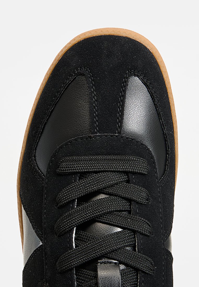 Sneaker nera con un mix di materiali in camoscio e pelle, punta rotonda, lacci neri e suola in gomma gommata testurizzata.