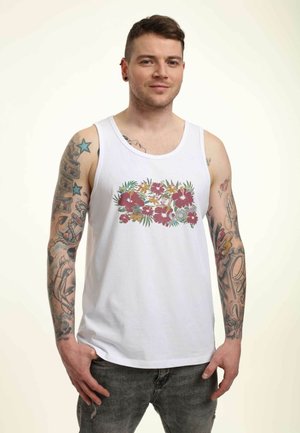Hvid bomulds tanktop med et blomstermotiv med pink, grønne og gule blomster, båret med mørkegrå jeans.