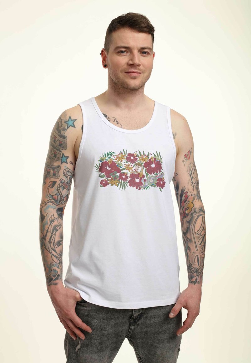Vit bomullstopp utan ärmar med ett blommönster i rosa, gröna och gula blommor, kombinerad med mörkgrå jeans.