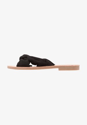 Zwarte zachte stof slip-on sandaal met een gedraaide uitstraling, lichte bruine platte zool en een minimalistische stijl zonder zichtbare hardware.