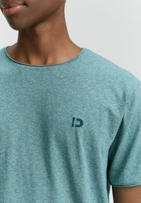 Svijetloplavi kratkotrajni rukav T-shirt s heathered teksturom. Ima okrugli izrez i mali tamnoplavi logo na lijevoj strani prsnog dijela.