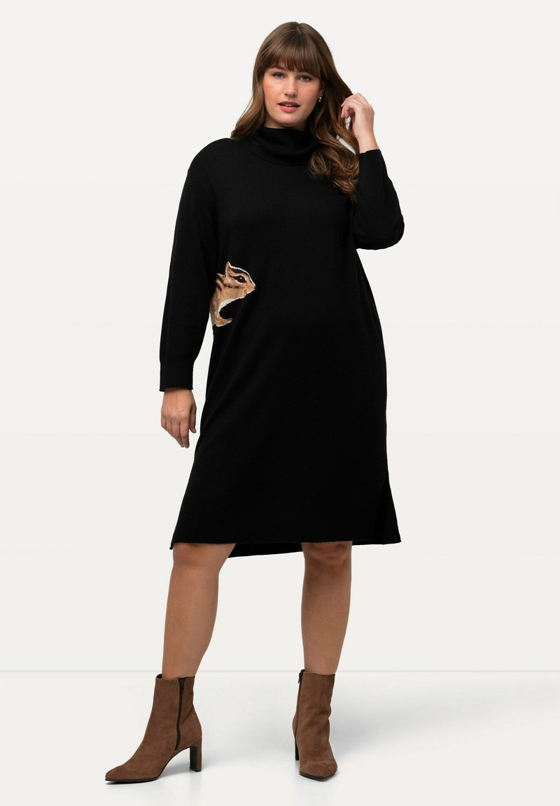 Vestito lungo nero a maglia con colletto alto, caratterizzato da un design di animale ricamato sul lato. Indossato con stivali alla caviglia marroni.