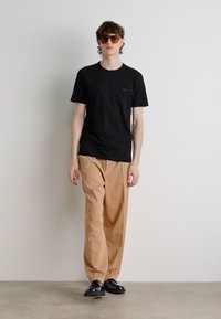 Čierne tričko, béžové voľné nohavice, čierne topánky a hnedé slnečné okuliare. Minimalistický dizajn s krátkymi rukávmi a malým logom na tričku.