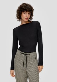 Langärmliges schwarzes Oberteil aus Stretchstoff, kombiniert mit karierten Hosen in Creme und Schwarz, die über einen Kordelzugbund und Seitentaschen verfügen.