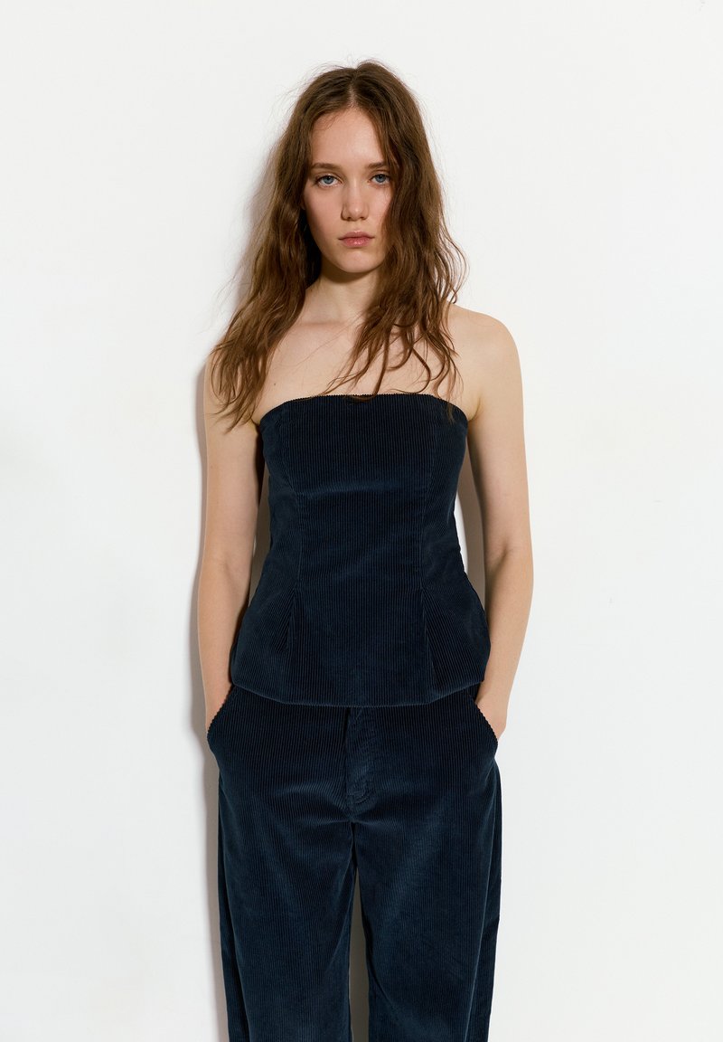 Mornarica kord neugodna bez naramenica s definiranim dizajnom, detaljima u obliku proširenih šavova i glatkom teksturom; u kombinaciji s odgovarajućim hlačama.