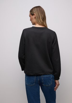 Pull-over matelassé noir avec un col rond et des manches longues, doté d'un tissu texturé et d'une coupe décontractée, associé à un jean denim bleu.