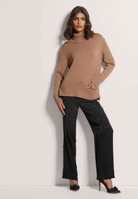 Hellbrauner Rollkragenpullover mit geripptem Saum und Bündchen, kombiniert mit schwarzen weitgeschnittenen Hosen mit feiner Textur und schwarzen Absatzschuhen.