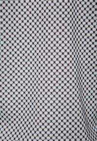 Tessuto di cotone con un motivo geometrico ripetitivo di piccole croci marroni su uno sfondo bianco, con una superficie liscia.