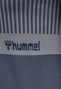 Close-up af blå og grå strikket stof med lodrette striber og "hummel" logo med et stiliseret humlemønster.