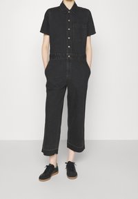 Svart denimjumpers med korta ärmar, krage, framknappar och bröstficka. Avskurna ben med rå kant. Matchas med svarta sneakers.