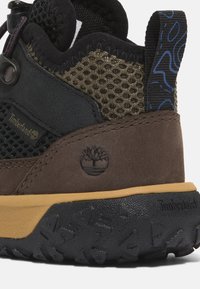 Hnědé a černé turistické boty s horní částí z jemné síťoviny a broušené kůže, gumová podešev, hexagonální vzor a logo Timberland. Viditelný nastavovací systém šněrování.