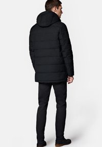 Czarna kurtka puchowa z kapturem, pikowana, o średniej długości. Noszona na czarnych spodniach i butach, widziana z tyłu.