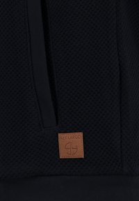 Navyblauwe sweatshirt met gestructureerde weving, een capuchon en een leren logopatch met de tekst "KEY LARGO" aan de voorkant. Heeft een gespleten zakontwerp.
