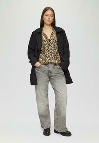 Schwarzer Trenchcoat über einer Bluse mit Leopardenmuster, kombiniert mit hellgrauen Jeans und schwarzen Ankle Boots. Glatte Stoffe, lockere Passform und lässiger Stil.