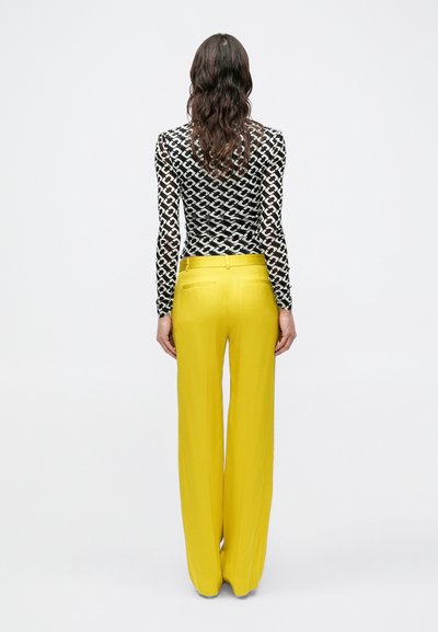 Zwart-witte top met lange mouwen en geometrisch patroon, gecombineerd met felgele, wijd uitlopende broek. Soepele stof met een getailleerde pasvorm.