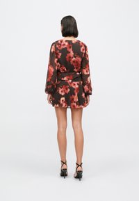 Vestido con estampado floral en tela oscura, con mangas largas y falda acampanada. El diseño incluye flores rojas vibrantes sobre un fondo negro.