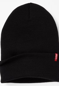 Black knit beanie with a folded cuff. Made of soft, textured fabric. Features a small red Levi's logo tag on the side.