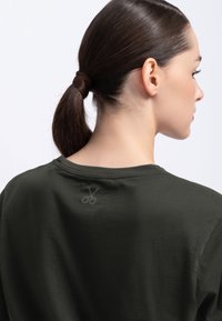 Donkergroene t-shirt met een ronde halslijn, voorzien van een subtiele schaarafbeelding op de bovenrug. Gemaakt van katoen met een relaxed fit.