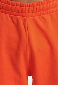 Orange sweatpants feature a soft, stretchy fabric with an elastic waistband and smooth texture, designed for comfort and ease of movement.