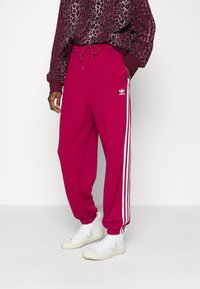 Rosa fleece-joggers med vita sidostråkar, med elastisk midja och fickor, i kombination med vita sneakers.