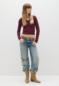 Burgunderfarbener, kabelgestrickter, cropped Pullover, zerstörte hellblaue Jeans, brauer Gürtel und beigefarbene, knöchelhohe Stiefeletten mit spitzen Zehen.