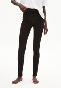 Jeans skinny de mezclilla negra de tiro alto con cuatro bolsillos, cierre de botón y textura suave. El diseño ajustado realza la silueta.