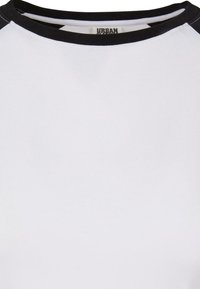 Vit T-shirt med rund svart halsringning och svarta kortärmar. Slät bomullstextur. Urban varumärkesetikett nära kragen.