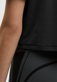 Fekete atlétikai póló egyenes szegéllyel, rövid ujjakkal és egy finom logó részlettel. Testhezálló, sima textúrájú fekete leggingszel viselve.