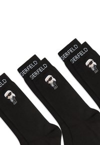 Calzini neri con logo bianco a contrasto raffigurante una figura con occhiali da sole. Hanno una texture liscia e polsini a costine.