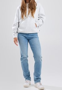 Grå huvtröja med ficka fram, sammansatt med ljusblå jeans och vita sneakers. Tyget ser mjukt ut med en avslappnad passform.