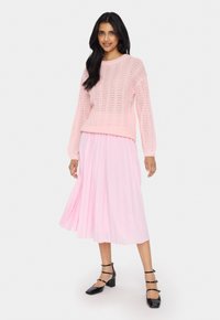 Light pink knitted sweater with a textured pattern and ribbed hem paired with a flowing light pink pleated midi skirt. Black block-heeled shoes.
