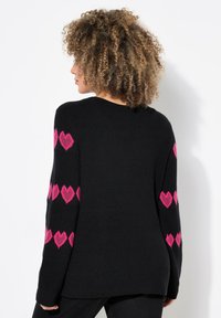 Maglione nero a maglia con motivi a cuori rosa sulle maniche, dotato di una texture a coste e un design rilassato.