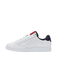 Zapatillas deportivas blancas hechas de cuero suave con diseño perforado, con talón acolchado en azul marino y acento rojo en la lengüeta. Suela de goma.