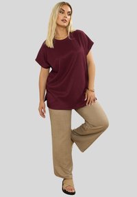 Burgundowa, prążkowana koszulka z krótkim rękawem, w połączeniu z beżowymi szerokimi spodniami i czarnymi sandałami. Prosty, luźny krój i fakturowana tkanina.