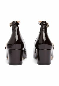 Botines de charol negros con tacón de bloque, correa ajustable con hebilla dorada y un acabado suave y brillante.