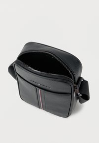 Μαύρο δερμάτινο τσάντα χιαστί με υφή, κλείσιμο με φερμουάρ και μπροστινή τσέπη με οριζόντιο ριγέ μοτίβο σε κόκκινο, λευκό και μπλε.