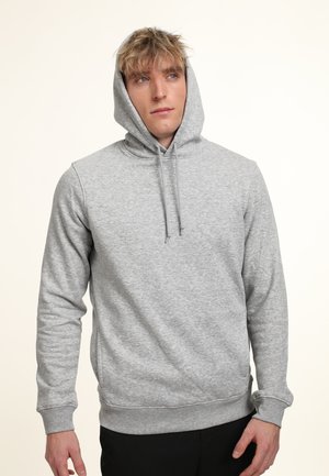 Gray hooded sweatshirt made of soft, textured fabric. Features a drawstring hood and ribbed cuffs and hem. Model stands with hands relaxed.