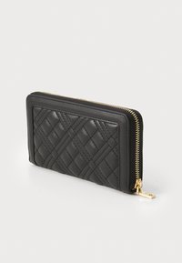 Carteira de couro preta com quilted e fecho de correr dourado, apresentando uma forma retangular e superfície texturizada. Destacada com um detalhe de puxador de fecho.