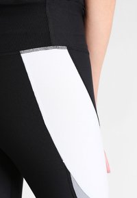 Leggings neri con un pannello bianco e grigio di lato, caratterizzati da una texture liscia e cuciture a contrasto lungo le cuciture.