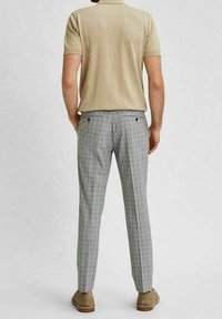 Beige polo tričko, šedé kostkované kalhoty s přizpůsobeným střihem a světle hnědé boty. Látka vypadá hladce s strukturovaným designem.