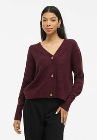 Cardigan en tricot bordeaux avec un col en V, des manches longues et cinq boutons à l'avant. Texture côtelée avec une coupe courte.