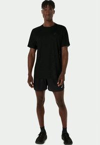 Svart treningst-skjorte med rund hals, parret med svarte shorts med logo. Stoffet har en lett, pustende tekstur.