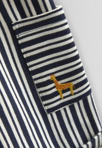 Prúžkovaná látka s námorníckymi modrými a bielymi vodorovnými pruhmi. Obsahuje vrecko s vyšitou žirafou v žltých a oranžových odtieňoch.