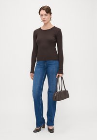 Camisola castanha de mangas longas, jeans azuis com corte evasé e uma pequena bolsa escura. O conjunto apresenta um design simples e uma textura suave.