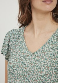 Roheline lilleline topp V-kaeluse, lühikeste libisevate varrukate ja kerge, tekstureeritud kangaga, millel on valged ja oranžid lilled.